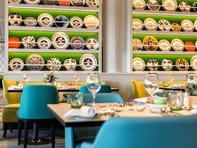 Ein helles, modernes Restaurant an Bord der Mein Schiff 6 mit mehreren Tischen, bereit für Gäste. Dekorative Teller zieren grüne Wände.