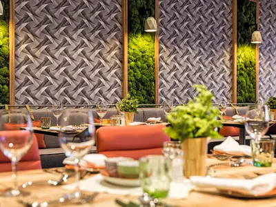 Einblick in das moderne Restaurant an Bord der Mein Schiff 6. Die Tische sind gedeckt mit Besteck und Gläsern. Im Hintergrund eine Wand mit geometrischem Muster und grünen Pflanzenpaneelen.