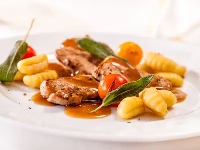 Appetitlich angerichtetes Gericht an Bord der Mein Schiff 6 mit Fleisch in Soße, Gnocchi, Kirschtomaten und Salbei auf weißem Teller.