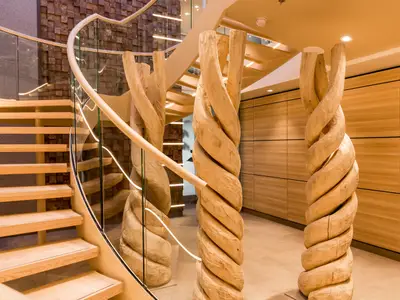 Modernes Atrium an Bord der Mein Schiff 6. Geschwungene Holztreppe mit Glasgeländer und LED-Beleuchtung. Imposante, spiralförmige Holzsäulen. Warme Holzpaneele an den Wänden.