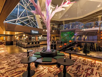 Innenansicht des japanischen Spezialitätenrestaurants Hanami an Bord der Mein Schiff 6. Ein kunstvoller rosa Baum dominiert den Raum mit Bar, Tischen und einer Felsengarten-Landschaft.