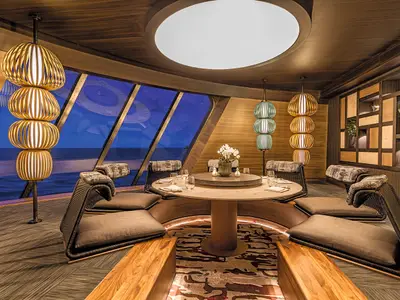 Das Spezialitätenrestaurant Hanami - By Tim Raue an Bord der Mein Schiff 6. Elegantes Interieur mit Holzelementen, runden Tischen, Sesseln und Panoramafenstern zum Meer.