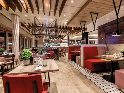 Die Osteria an Bord der Mein Schiff 6. Ein modernes Restaurant mit roten Sitzbänken, gedeckten Tischen und offener Küche.