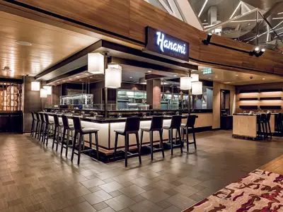 Innenansicht des Hanami by Tim Raue Spezialitätenrestaurants an Bord der Mein Schiff 6. Moderne Theke mit Barhockern, dunklem Tresen, Holzwände und warmes Licht schaffen ein elegantes Ambiente.