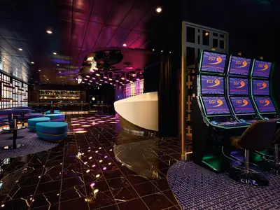 Blick in eine modern beleuchtete Lounge der Mein Schiff 7 mit Bar, Sitzgelegenheiten, einer Empfangstheke und einer Reihe von Spielautomaten an der Seite.
