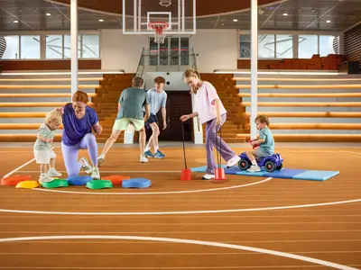 Eine Familie, bestehend aus Erwachsenen und Kindern unterschiedlichen Alters, betreibt Sport und spielt in der Arena an Bord der Mein Schiff 7. Es gibt verschiedene Spielbereiche und eine Zuschauertribüne im Hintergrund.
