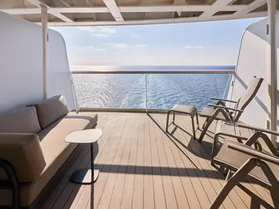Der helle Balkon einer Kabine an Bord der Mein Schiff Relax bietet ein Sofa, einen Tisch und zwei Stühle mit Blick auf das weite Meer und den blauen Himmel.