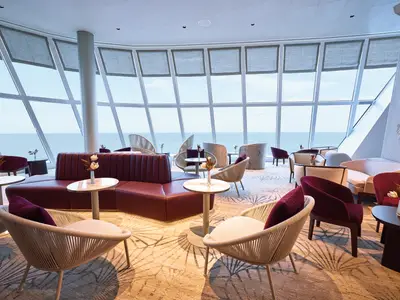 Geräumige Lounge an Bord der Mein Schiff Relax mit raumhohen Fenstern und Meerblick. Rote Ledersofas und helle Sessel laden zum Verweilen ein.