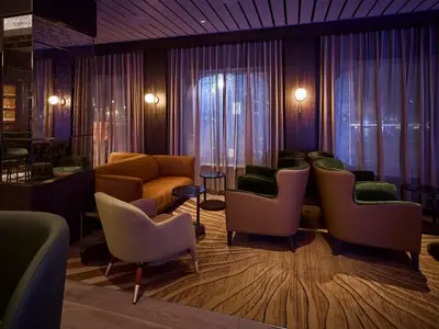 Eine elegant eingerichtete Lounge an Bord der Mein Schiff Relax. Komfortable Sessel, Sofas und Tische bieten gemuetliche Sitzbereiche; gedämpftes Licht schafft entspannte Atmosphäre.