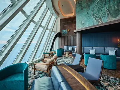 Die Captain's Bar an Bord der Mein Schiff Relax zeigt einen eleganten Loungebereich mit großen Fenstern zum Meer. Blaue Sitzmöbel, dunkles Holz und Kunst prägen das Interieur.