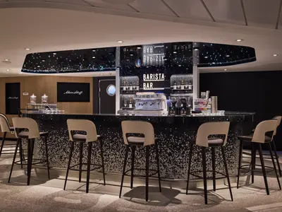 Moderne Barista Bar auf der Mein Schiff Relax. Lange Theke, Barhocker. Kaffeemaschine, Flaschenregale. Dunkle Decke mit Sternenlicht. Holzvertäfelte Wände mit Mein Schiff-Logos.
