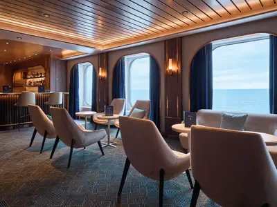 Elegante Bar-Lounge der Mein Schiff Relax. Komfortable Sitzgruppen, Meerblick und stilvolle Holzbar. Der warm beleuchtete Raum ist menschenleer.
