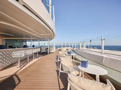 Die Bar 17 an Bord der Mein Schiff Relax: Eine stilvolle Outdoor-Bar mit Hockern, Loungebereich und weitem Panoramablick auf das offene Meer unter blauem Himmel.