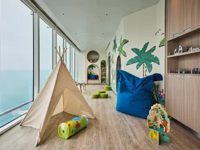 A vibrant 'Nest' baby room on Mein Schiff Relax, featuring a teepee, colorful jungle murals, and panoramic ocean views through large windows, designed for young children.