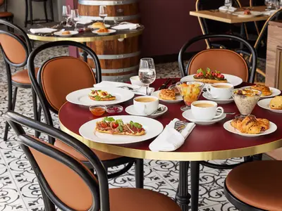 Französisches Frühstück im Sur Mer Bistrot der Mein Schiff Relax mit belegten Broten, Croissants, Müsli, Obstsalat und Kaffee. Eine elegante Einrichtung mit gemustertem Fliesenboden.