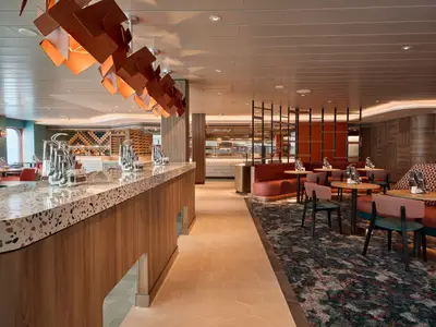 Modernes Mein Schiff Bistro auf der Mein Schiff Relax. Terrazzo-Theke, Holz-Lichtinstallation und Sitzbereiche mit Polstermöbeln und Tischen. Helles, einladendes Design.