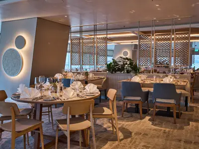 Modernes Restaurant X-Coast an Bord der Mein Schiff Relax. Elegant gedeckte Tische, stilvolle Einrichtung mit Wandbeleuchtung, Holzakzenten und gemusterten Raumteilern.