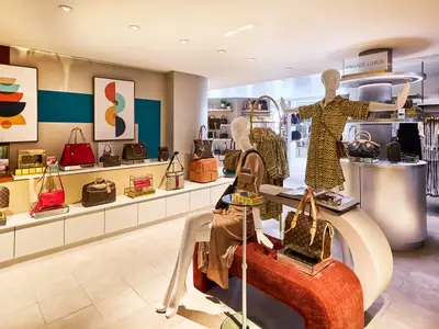 Ein heller, moderner Shop an Bord der Mein Schiff Relax präsentiert luxuriöse Vintage-Handtaschen und Damenkleidung auf Displays und Mannequins. Die Wände sind mit abstrakter Kunst dekoriert.