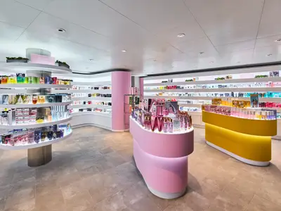 Ein weitläufiger, modern gestalteter Beauty-Shop an Bord der Mein Schiff Relax. Helle Regale und pinke sowie gelbe Theken präsentieren zahlreiche Parfüms und Kosmetikartikel.