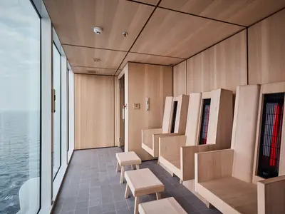 Moderner Infrarotsauna-Bereich an Bord der Mein Schiff Relax. Helle Holzeinrichtung, mehrere Sitzplätze mit roten Infrarotstrahlern und Blick auf das weite Meer.