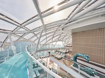 Heller, überdachter Deckbereich der Mein Schiff Relax mit blauer Jogging-Strecke und Sonnenliegen. Die moderne Glasarchitektur bietet Meerblick.