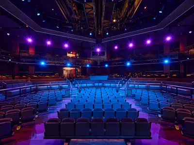 Innenansicht des Theaters an Bord der Mein Schiff Relax, gesehen von hinten, mit vielen leeren Sitzreihen in dunklen Farben und blau-lila Beleuchtung.